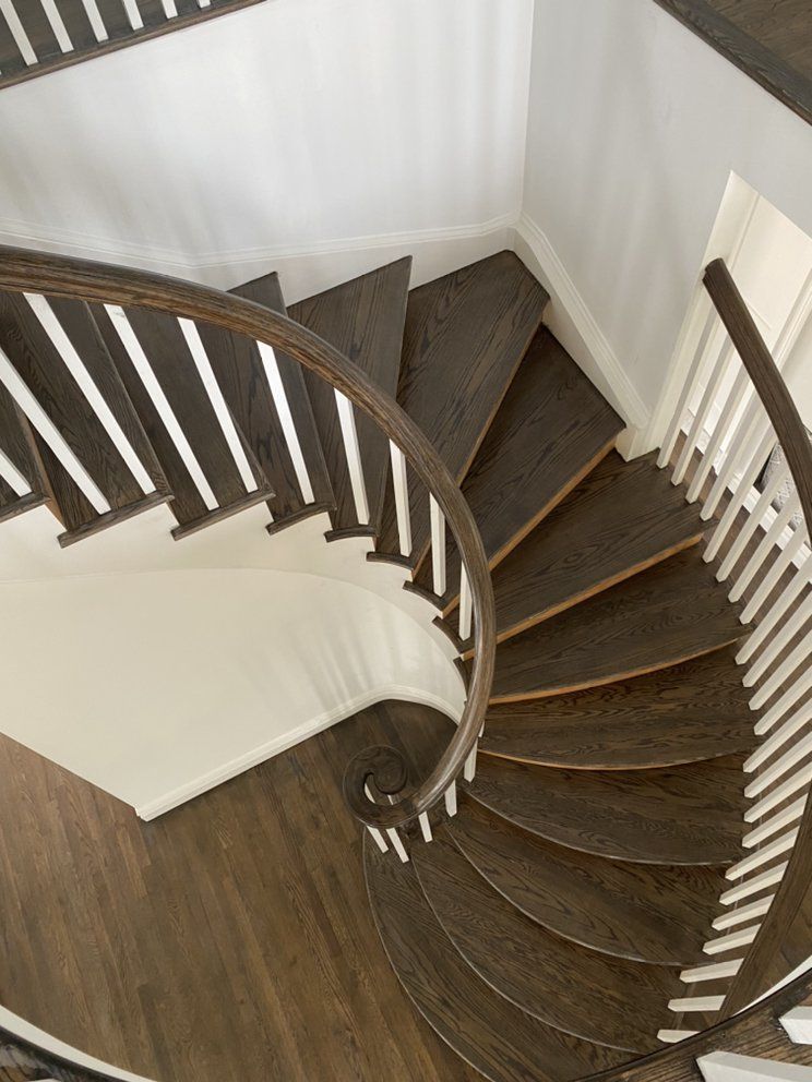 An aerial view of a spiral staircase with wooden steps and a white railing.