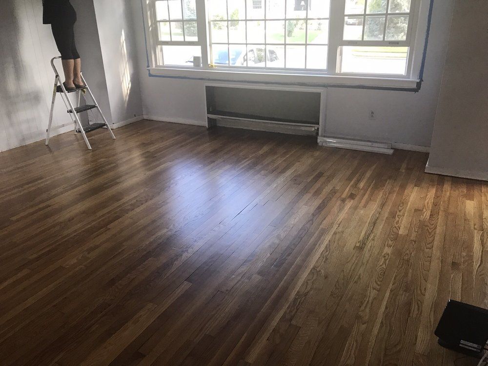 A person is standing on a ladder in a living room with hardwood floors.