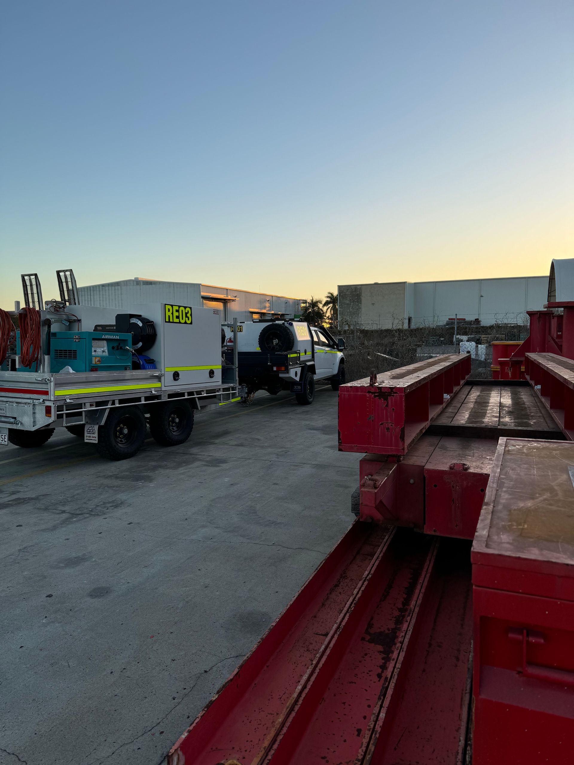 Construction site at dusk with blue utility truck, cement mixer, and red steel beams stacked in foreground — Resurge Diesel & Fabrication Pty Ltd In Balnagowan, QLD