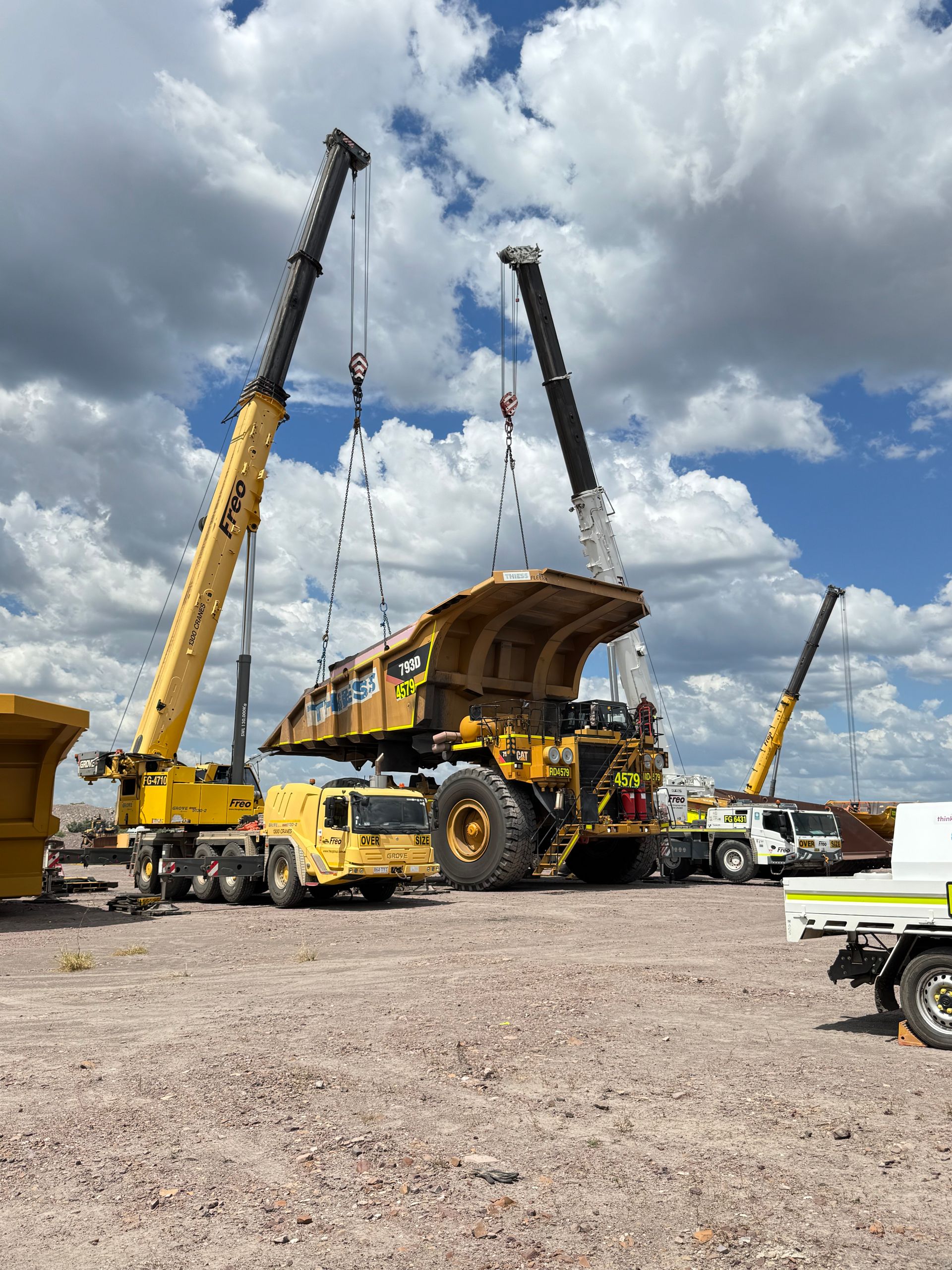 Yellow cranes lifting a giant mining dump truck in a gravel yard under cloudy skies — Resurge Diesel & Fabrication Pty Ltd In Balnagowan, QLD