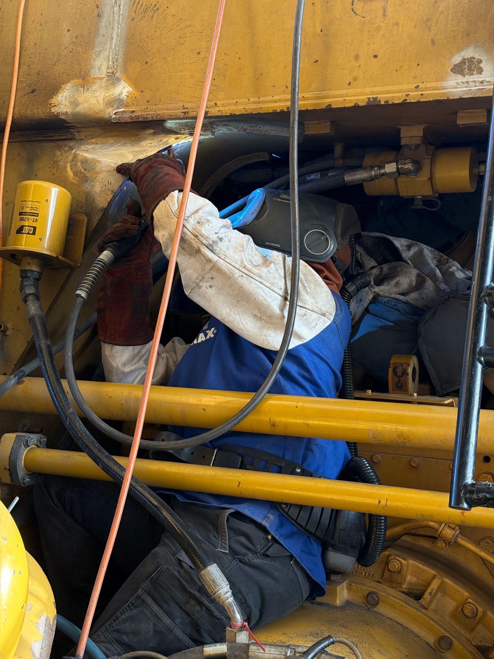 Worker in blue overalls crouches inside yellow machinery, inspecting or repairing components — Resurge Diesel & Fabrication Pty Ltd In Balnagowan, QLD