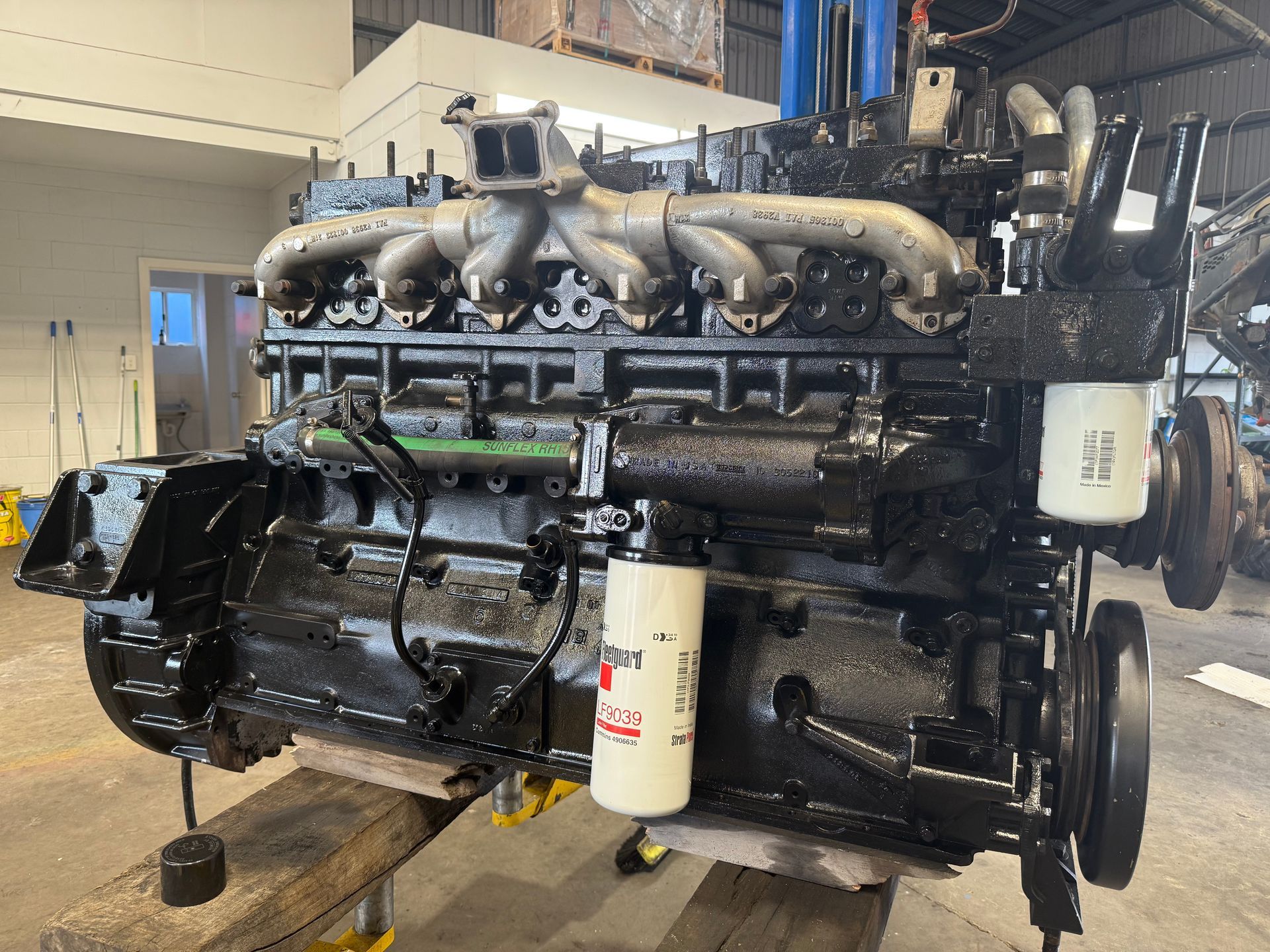 Large black industrial engine with pipes and filters, mounted on a wooden pallet in a workshop — Resurge Diesel & Fabrication Pty Ltd In Balnagowan, QLD