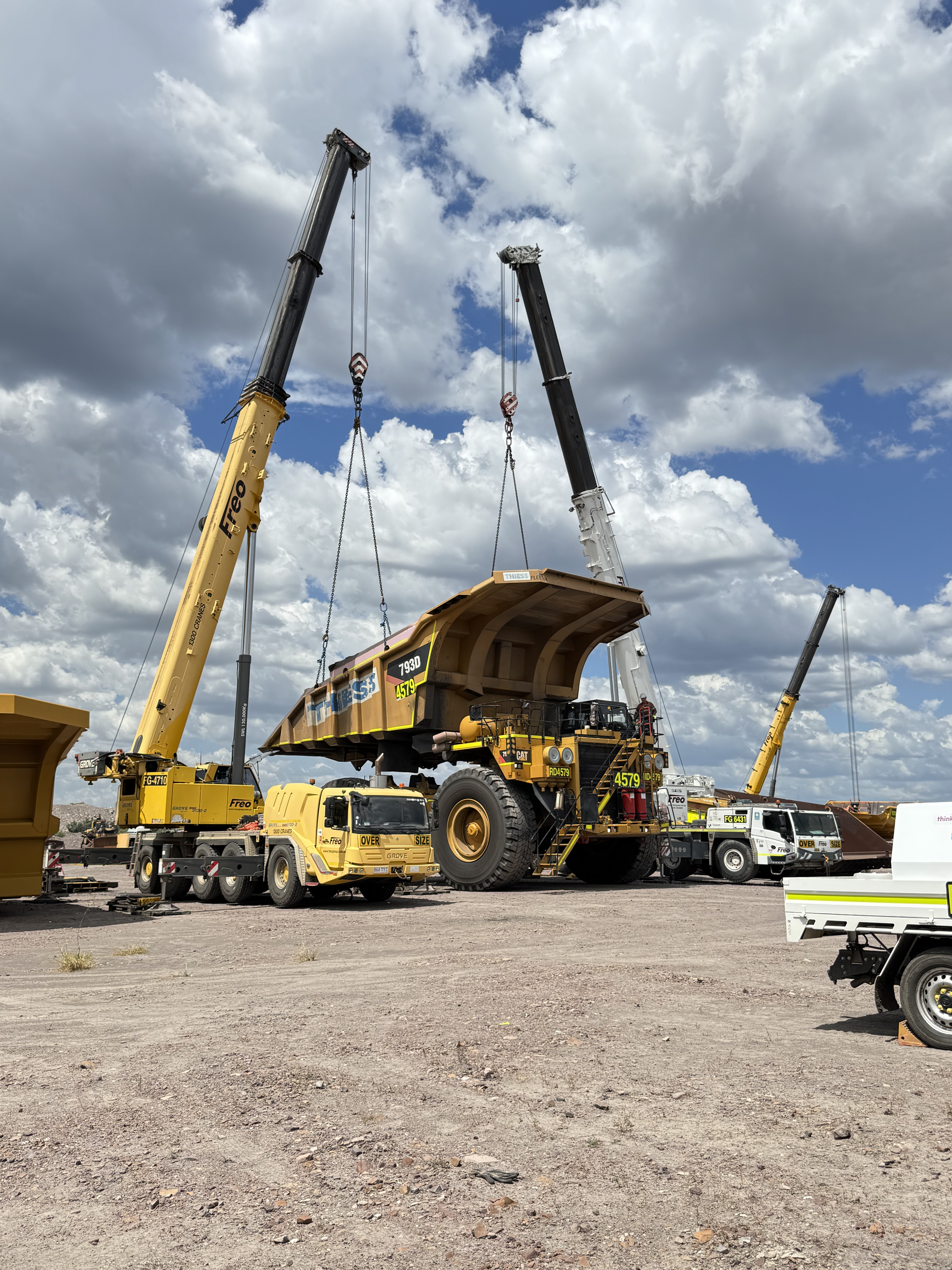 Heavy mining truck being lifted by two yellow cranes in a gravel yard under cloudy skies — Resurge Diesel & Fabrication Pty Ltd In Balnagowan, QLD