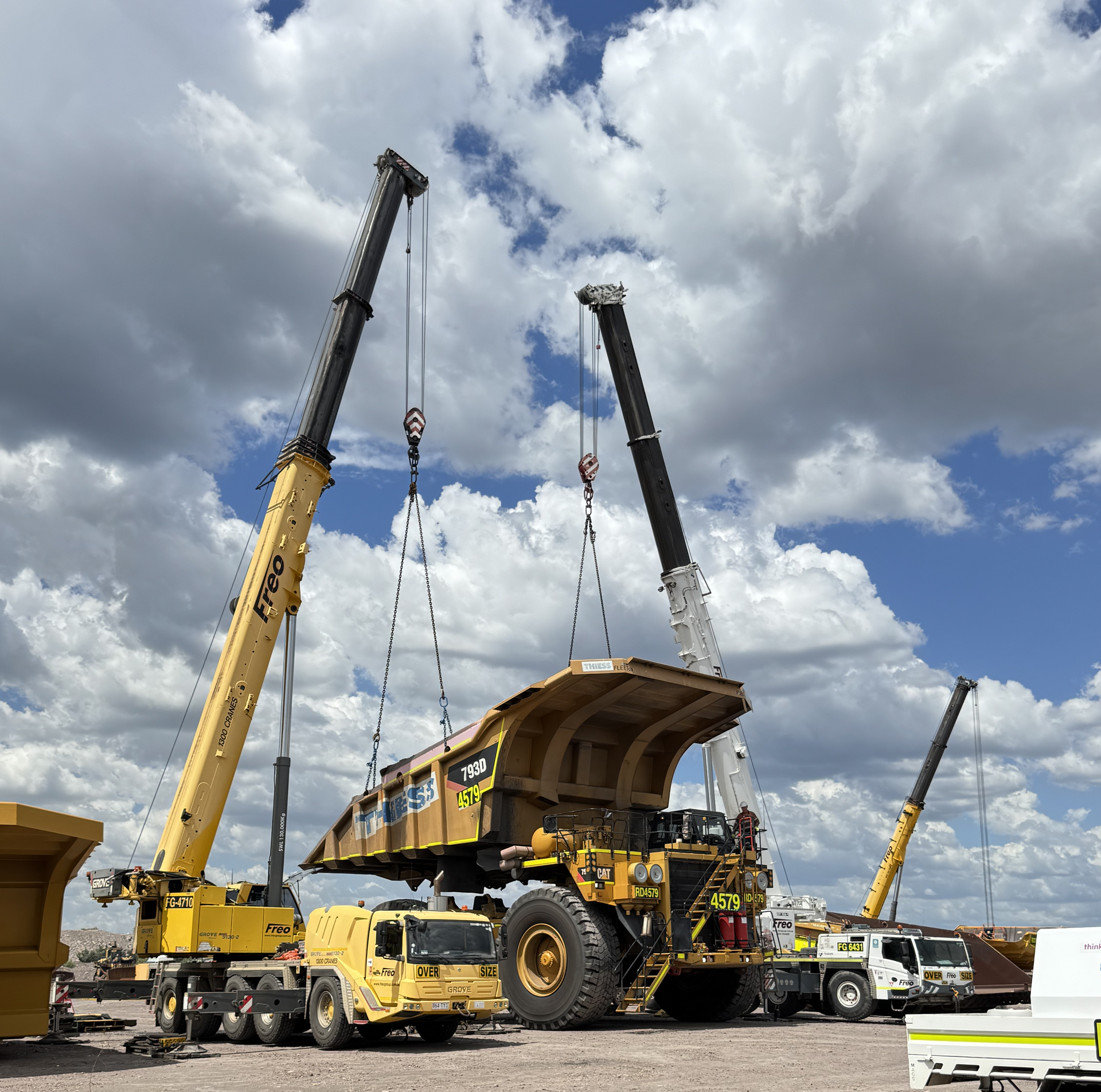 Two cranes lifting a large yellow mining truck bed under a cloudy sky at a construction site — Resurge Diesel & Fabrication Pty Ltd In Balnagowan, QLD