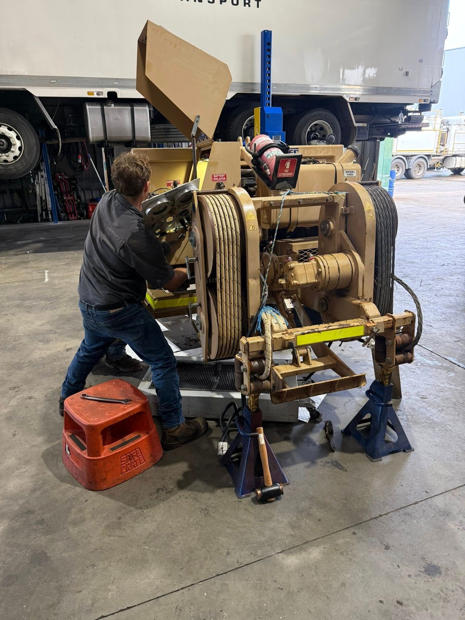 Mechanic in a workshop repairs a large machine with hoses and tools, standing beside a red stool — Resurge Diesel & Fabrication Pty Ltd In Balnagowan, QLD