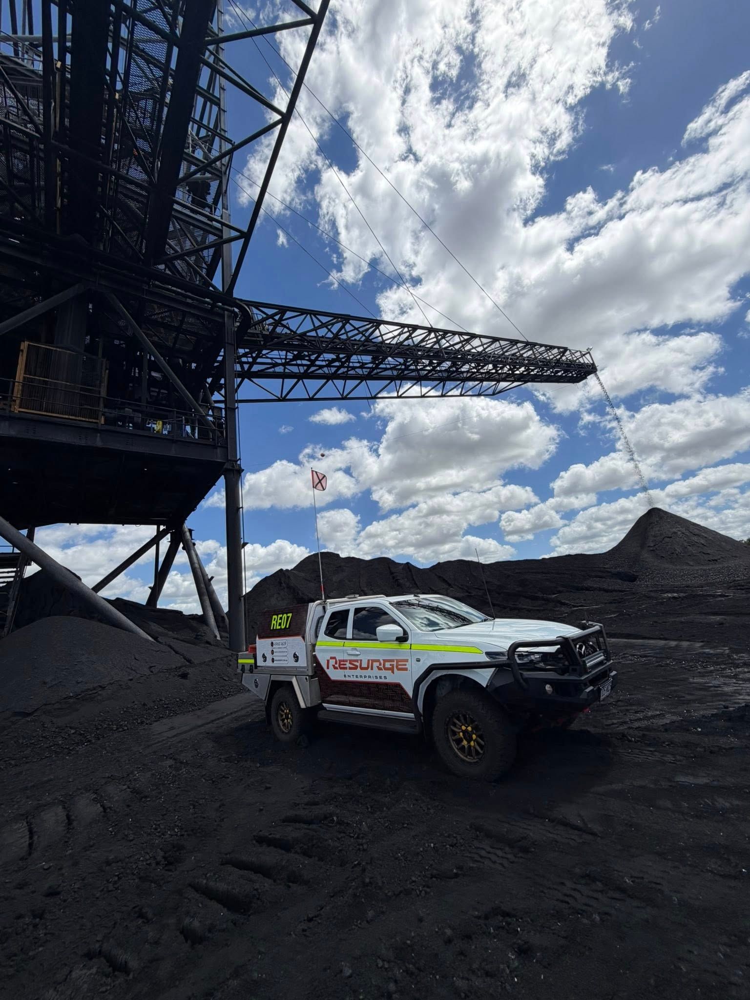 White off-road truck on black mining terrain beside a large conveyor structure under a cloudy blue sky — Resurge Diesel & Fabrication Pty Ltd In Balnagowan, QLD