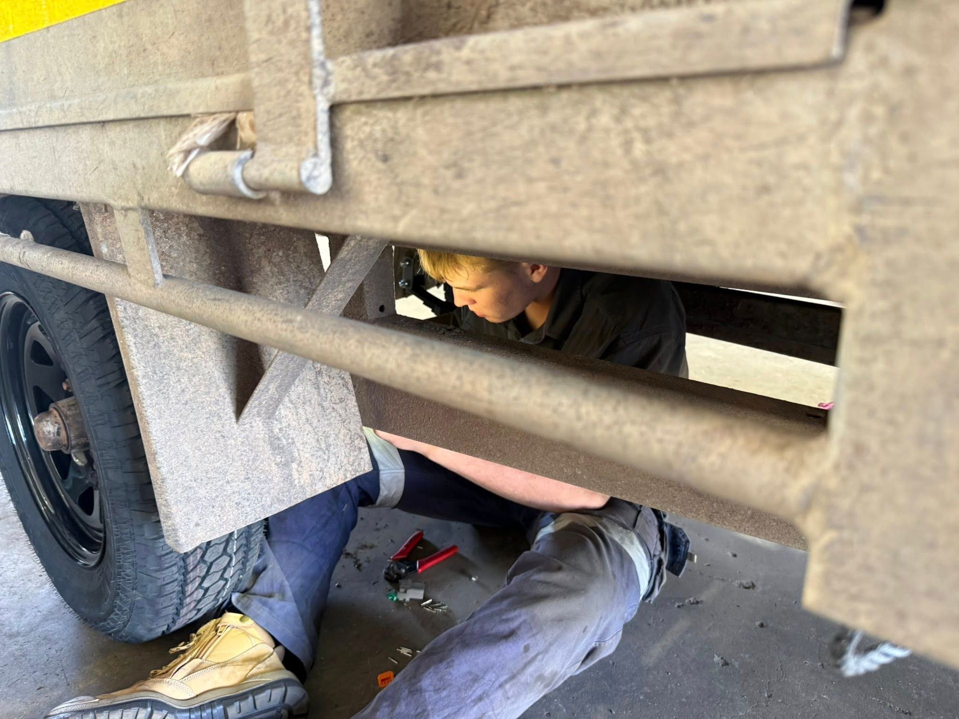 Mechanic lying under a vehicle, working near the rear wheel with tools on a garage floor — Resurge Diesel & Fabrication Pty Ltd In Balnagowan, QLD