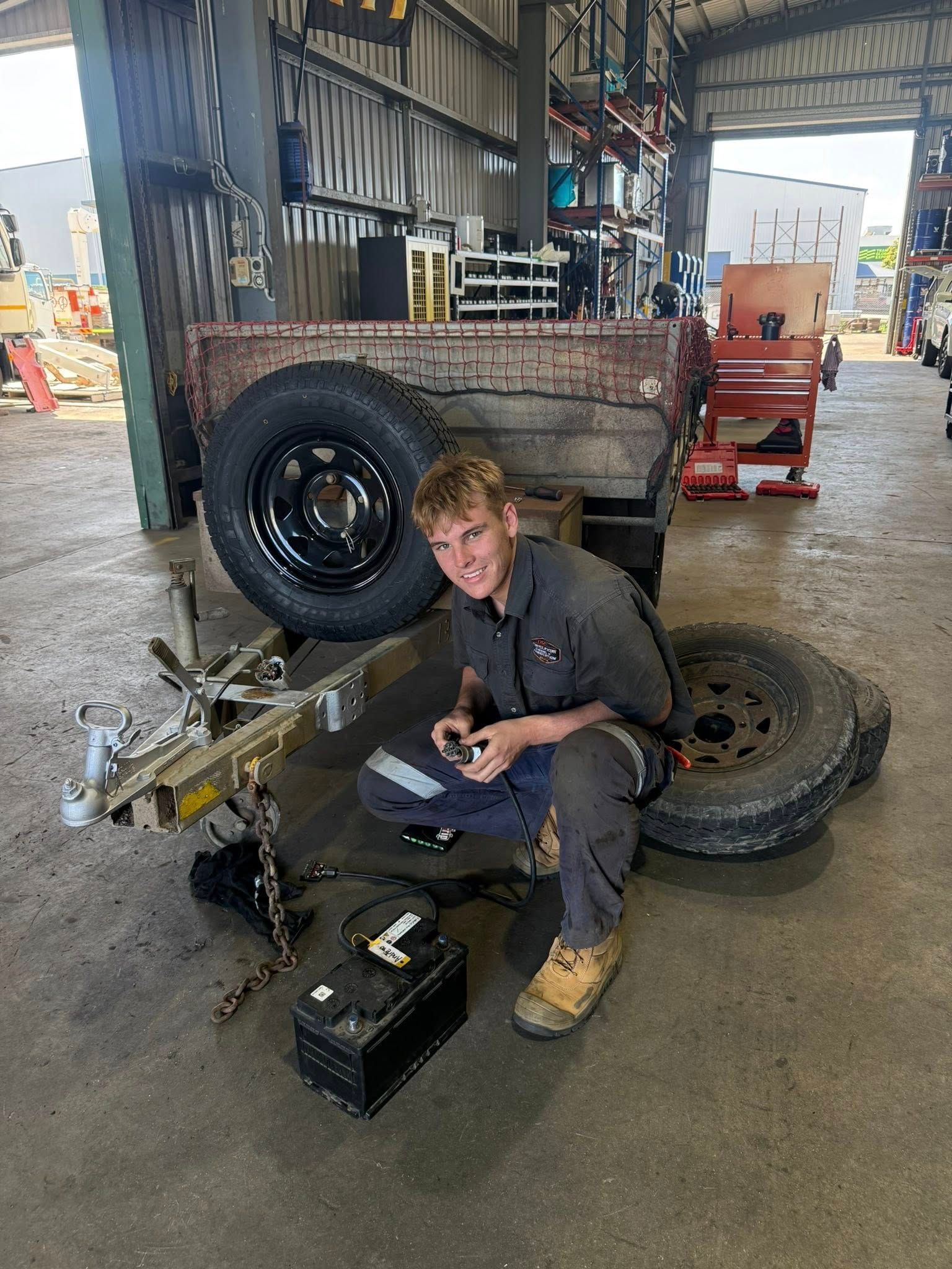 Mechanic kneeling in a garage beside a truck wheel and tools, repairing a tyre — Resurge Diesel & Fabrication Pty Ltd In Balnagowan, QLD