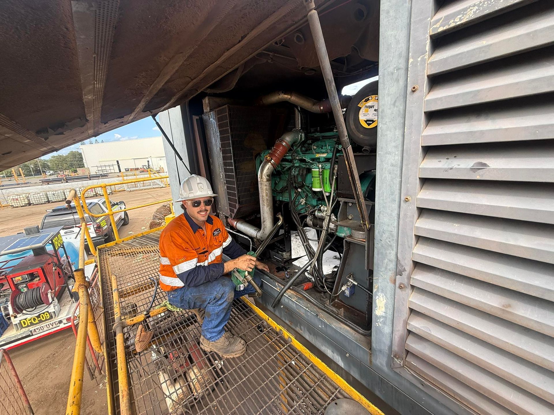 Worker in orange jacket inspecting machinery on a metal platform beside large industrial equipment — Resurge Diesel & Fabrication Pty Ltd In Balnagowan, QLD