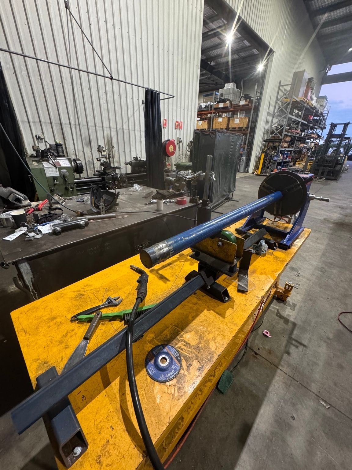 Yellow industrial machine on a workshop floor beside a metal workbench and stacked pallets — Resurge Diesel & Fabrication Pty Ltd In Balnagowan, QLD