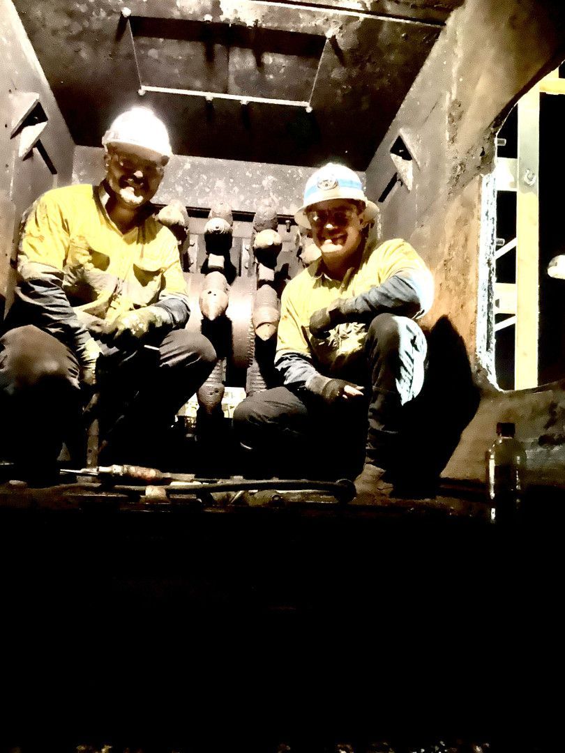 Two workers in hard hats crouch inside a dim industrial tunnel, smiling at the camera — Resurge Diesel & Fabrication Pty Ltd In Balnagowan, QLD