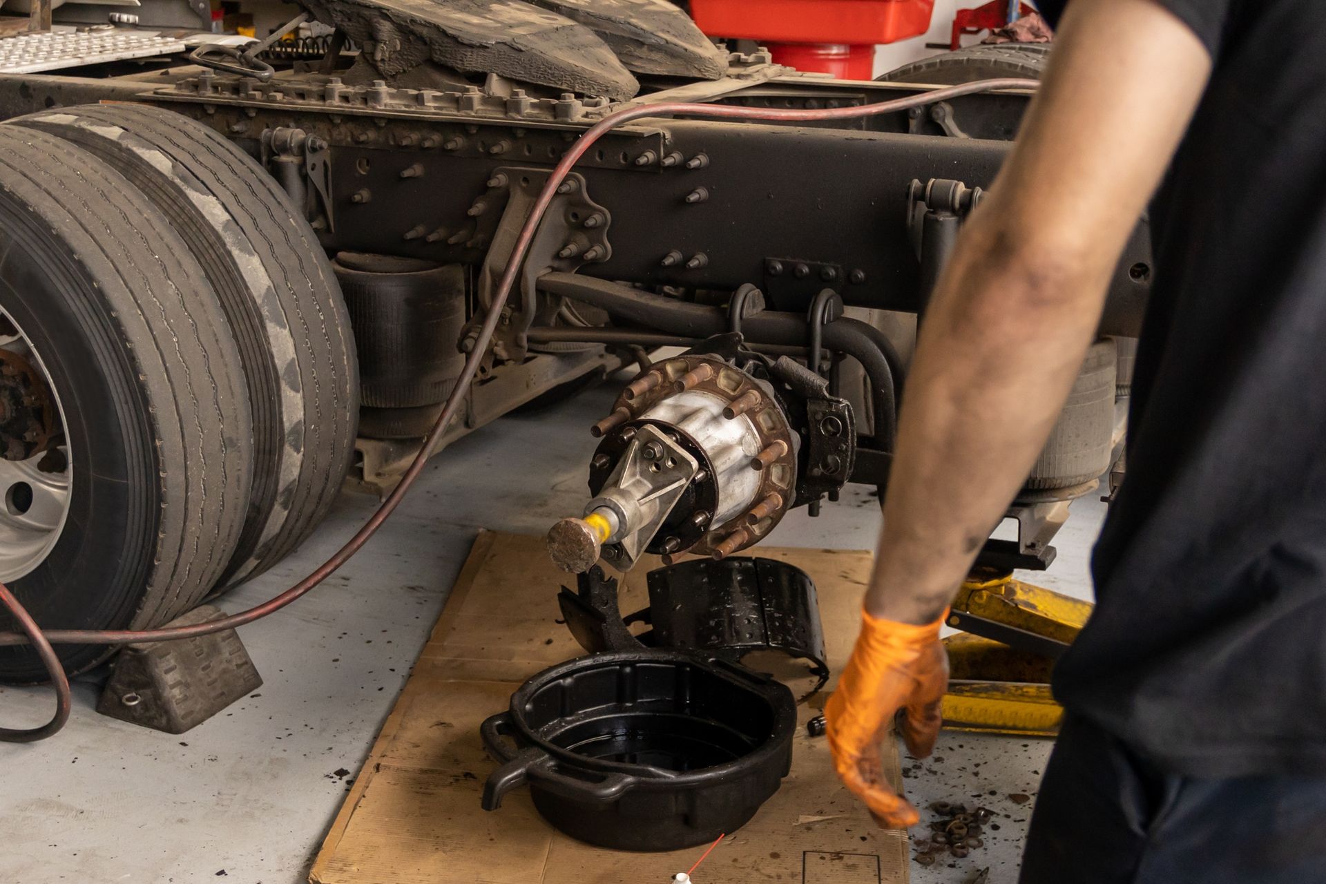 Mechanic Changing A Truck's Wheel Bearing. He's Wearing An Orange Glove And Holding Parts Over An Oil Pan In A Shop — Resurge Diesel & Fabrication Pty Ltd In Balnagowan, QLD