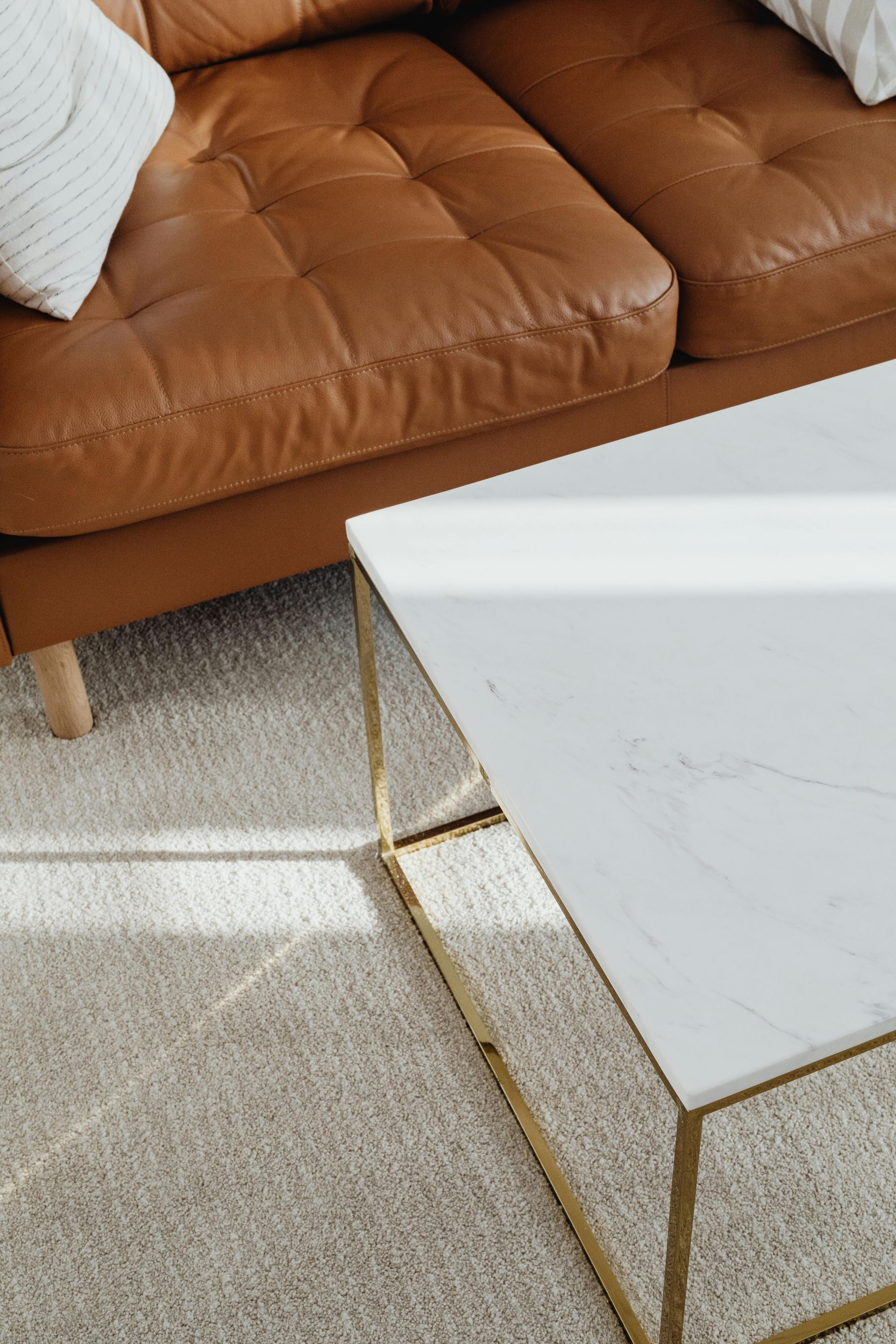 Brown leather sofa beside a white marble coffee table with a gold frame on a beige carpet.
