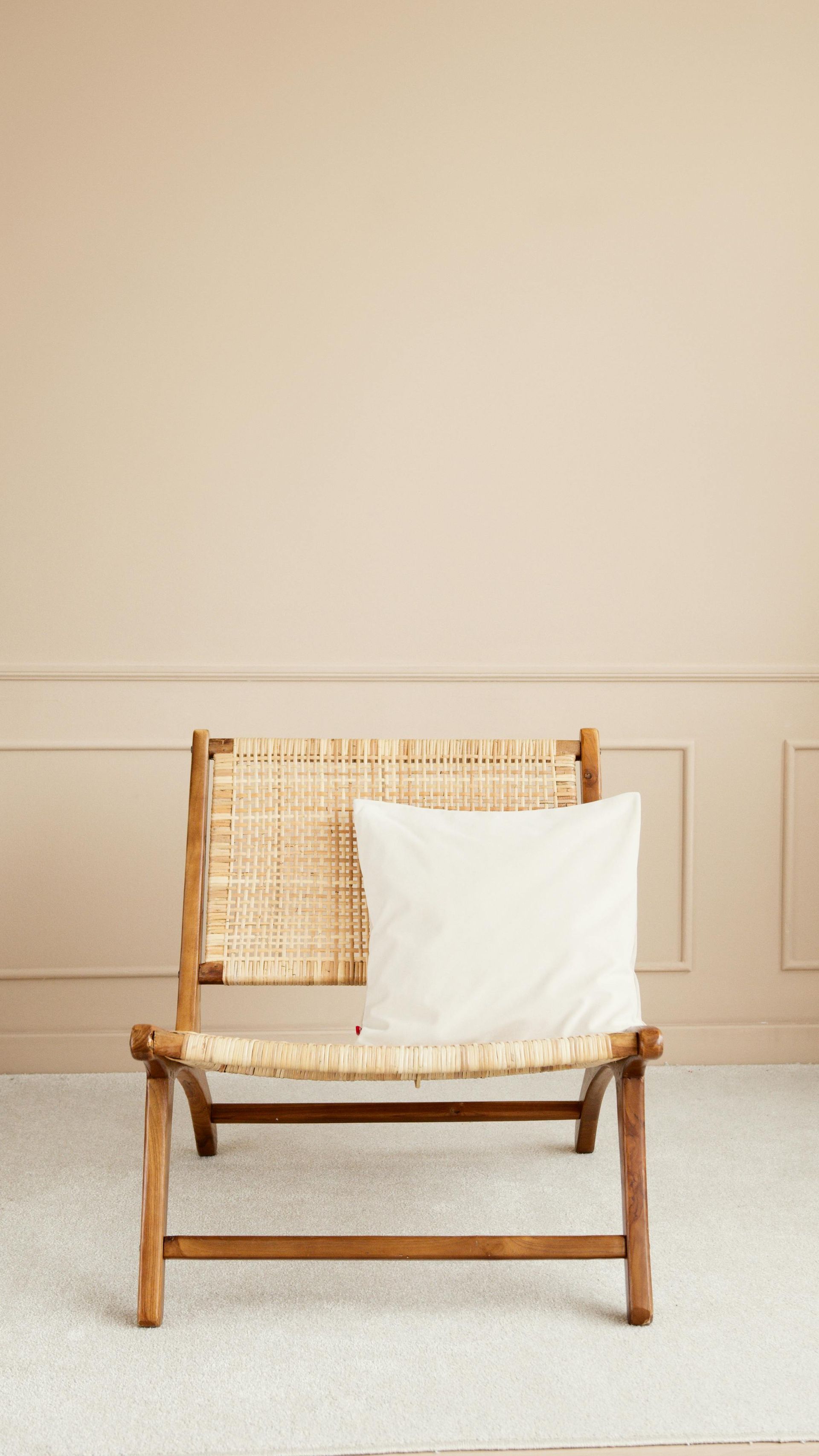 Wooden chair with woven back and a white pillow against a beige wall.
