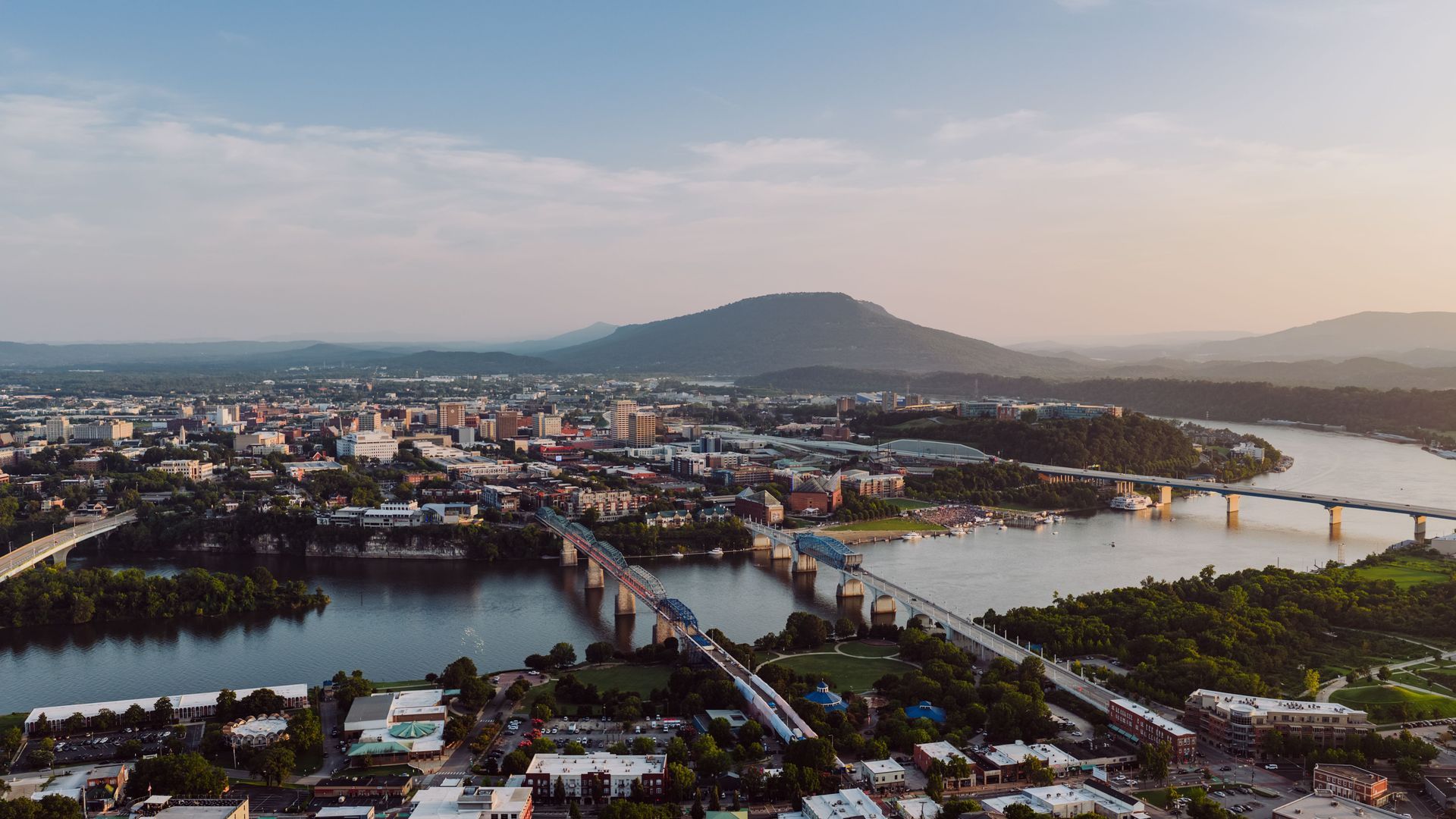 Aerial view of a city with bridges over a river and a mountain in the distance at sunset.