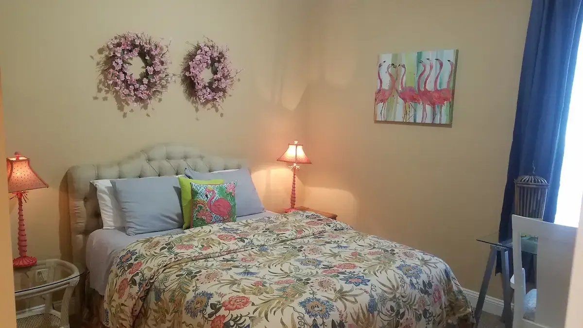 A bedroom with a bed , two lamps , two wreaths on the wall and a painting on the wall.