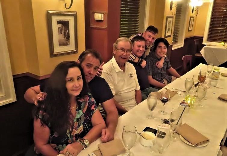Group of six seated at a warmly lit restaurant table, smiling for a dinner photo.