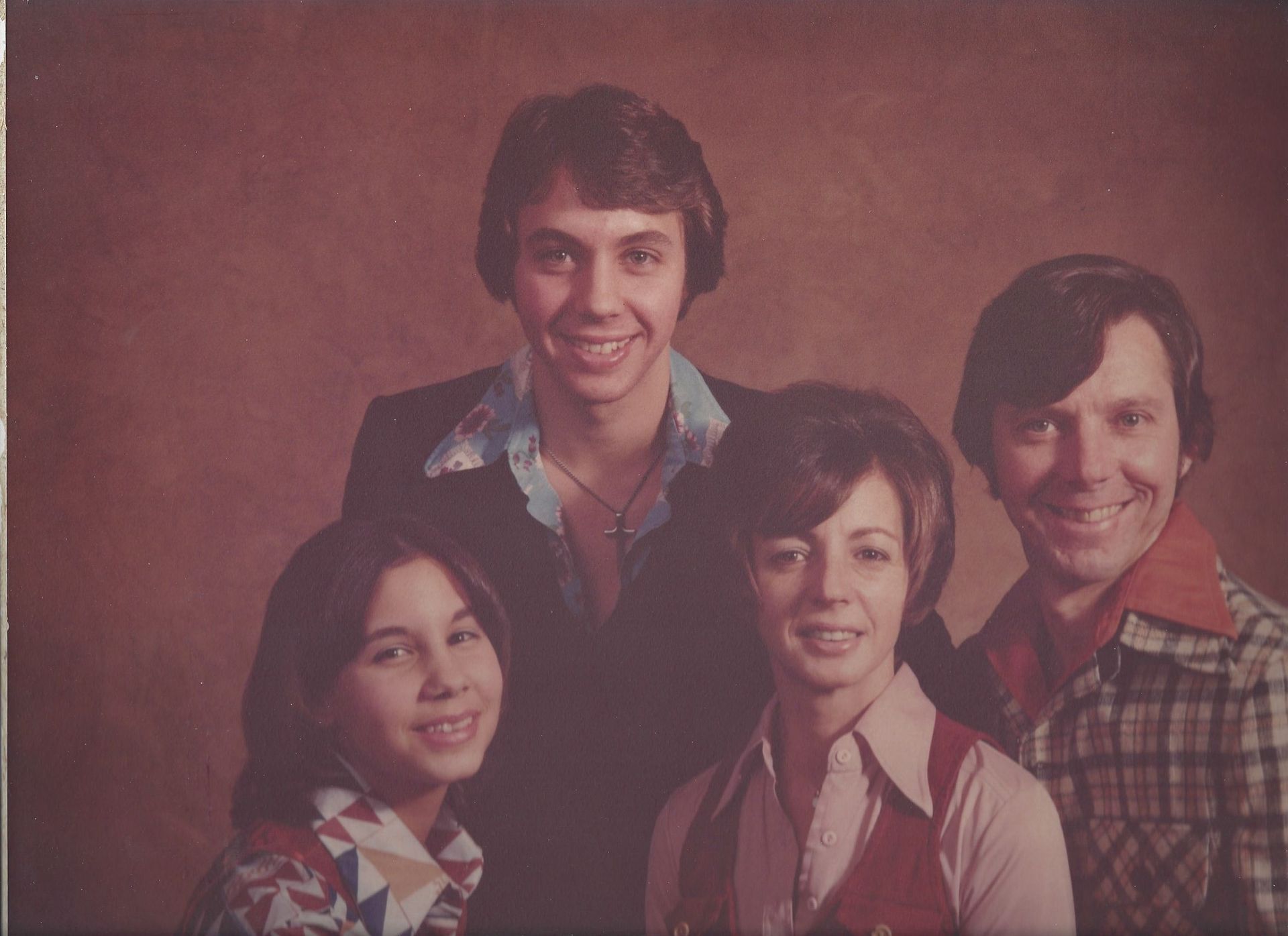 Four people posing together against a plain brown backdrop, smiling at the camera.