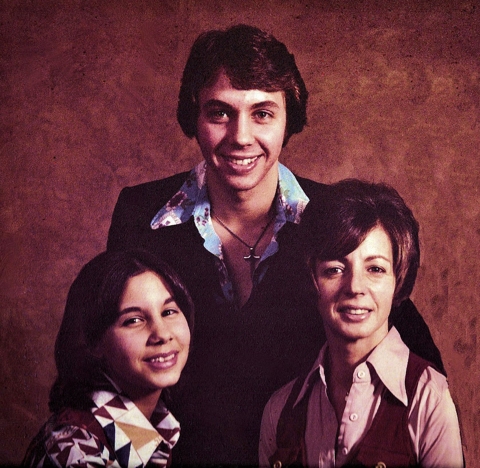 Three smiling people posed in a studio portrait against a brown backdrop.