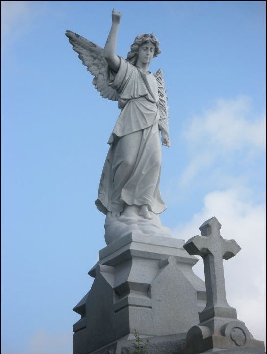 White angel statue with raised arm atop a stone monument against a blue sky