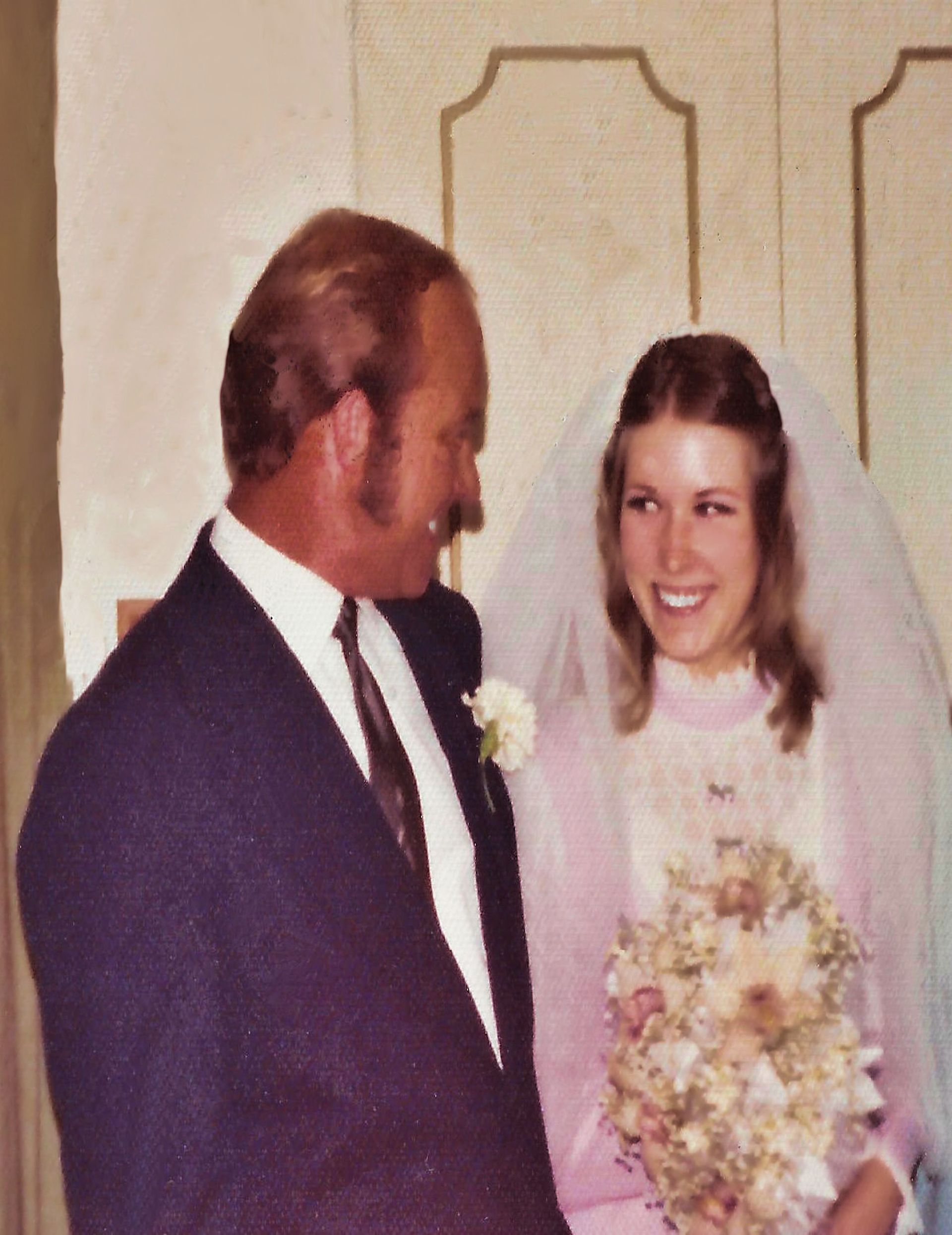 Wedding couple smiling, bride holding bouquet beside groom in dark suit and tie.