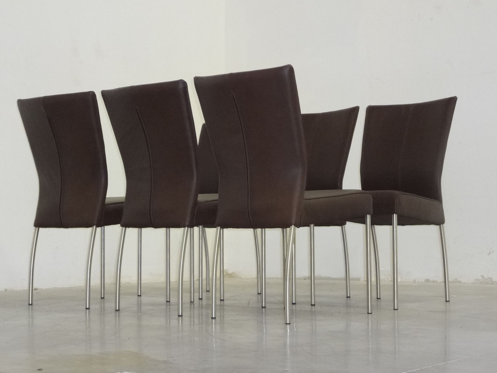 Zes donkergrijze eetkamerstoelen met hoge rugleuningen en zilverkleurige metalen poten