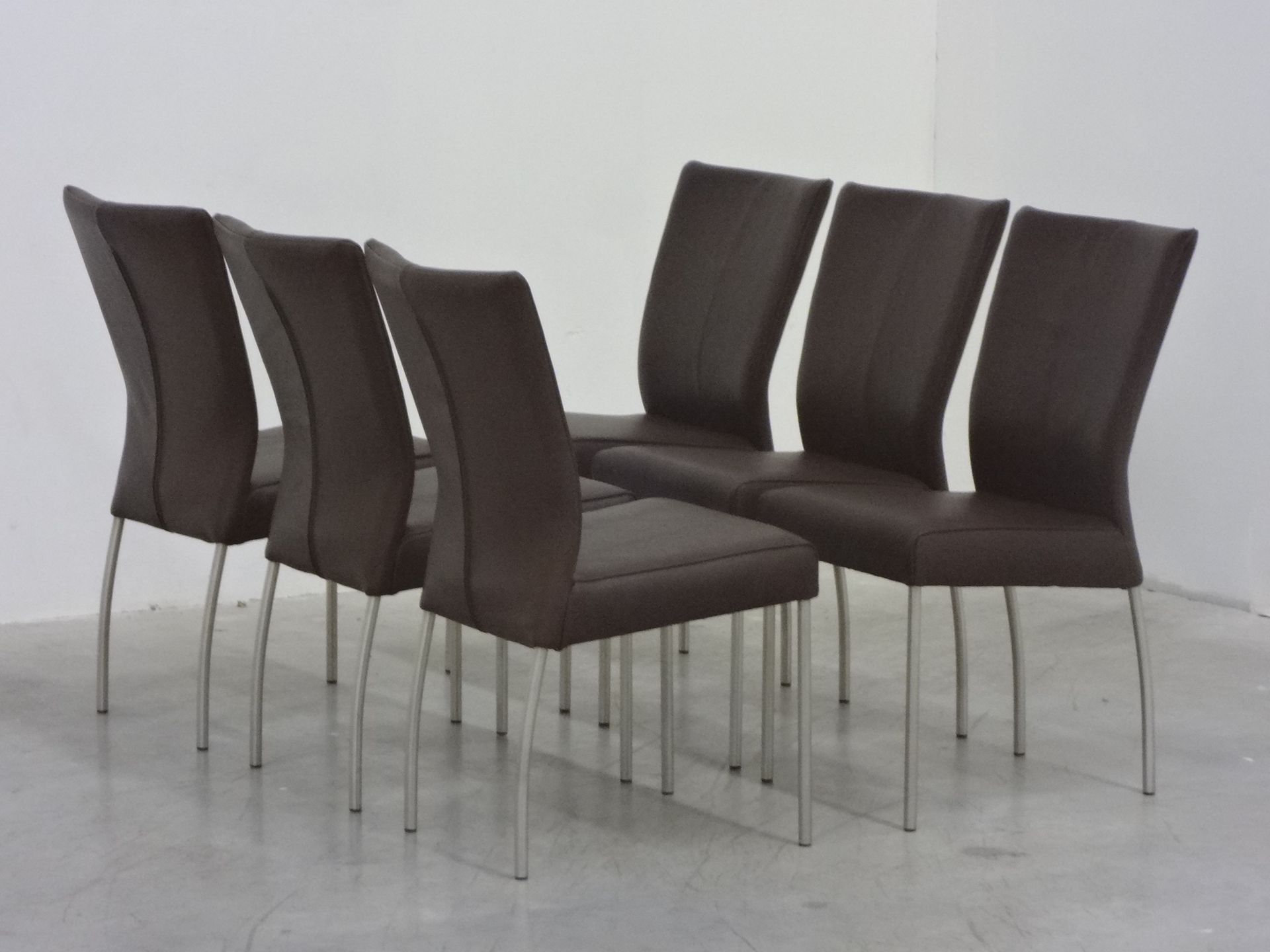 Zes donkergrijze eetkamerstoelen met hoge rugleuningen en zilverkleurige metalen poten