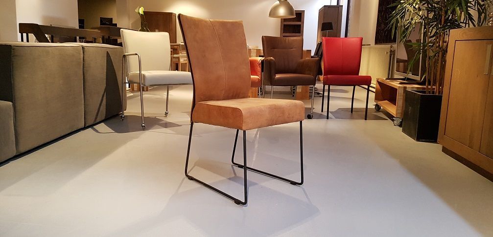 Een beige, gestoffeerde stoel met een dun metalen frame staat in een lichte, moderne meubelshowroom, omringd door andere 
