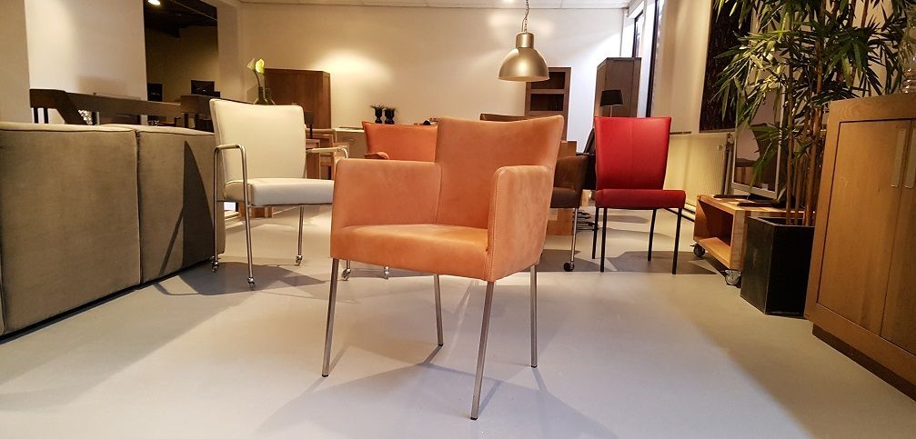 In een meubelshowroom staan ​​diverse moderne stoelen met metalen poten, waaronder oranje, witte en rode modellen.