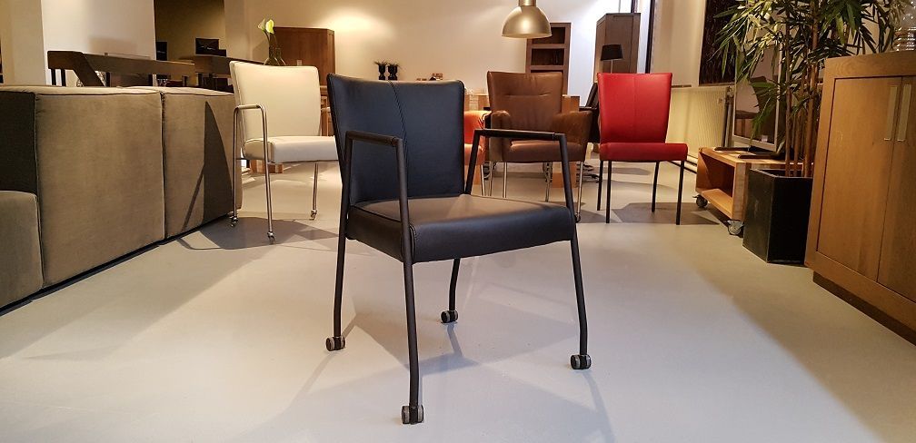 Een zwarte leren fauteuil staat centraal in een showroom van een meubelwinkel, met andere stoelen op de achtergrond.
