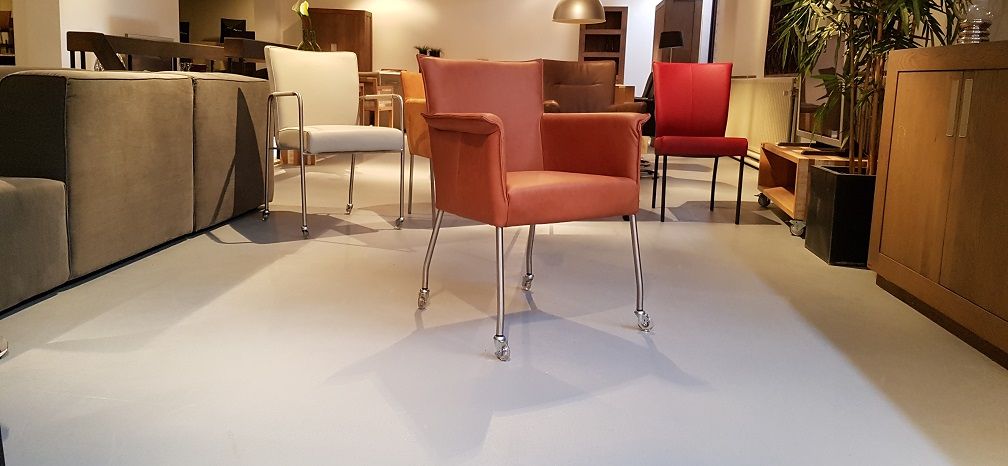 bruin cognac fauteuil met metalen poten staat centraal in een showroom , met andere stoelen  in het zicht.