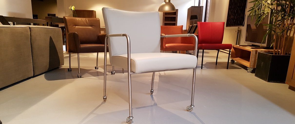 Een moderne, witte gestoffeerde stoel met een chromen frame staat op de voorgrond van een meubelshowroom.