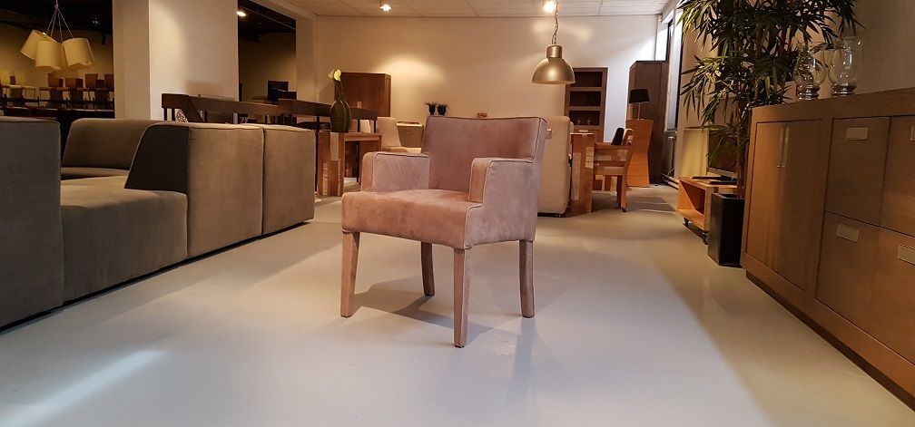 In het midden van een goed verlichte, moderne meubelshowroom staat een roze gestoffeerde stoel met houten poten.