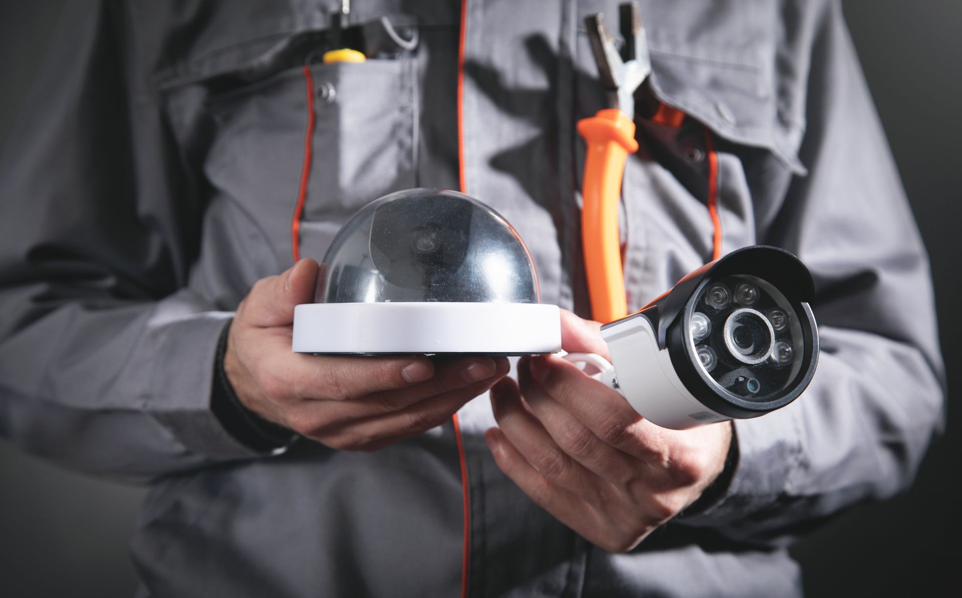 A technician holds two cameras in one hand, and a spanner is hanging on his shirt