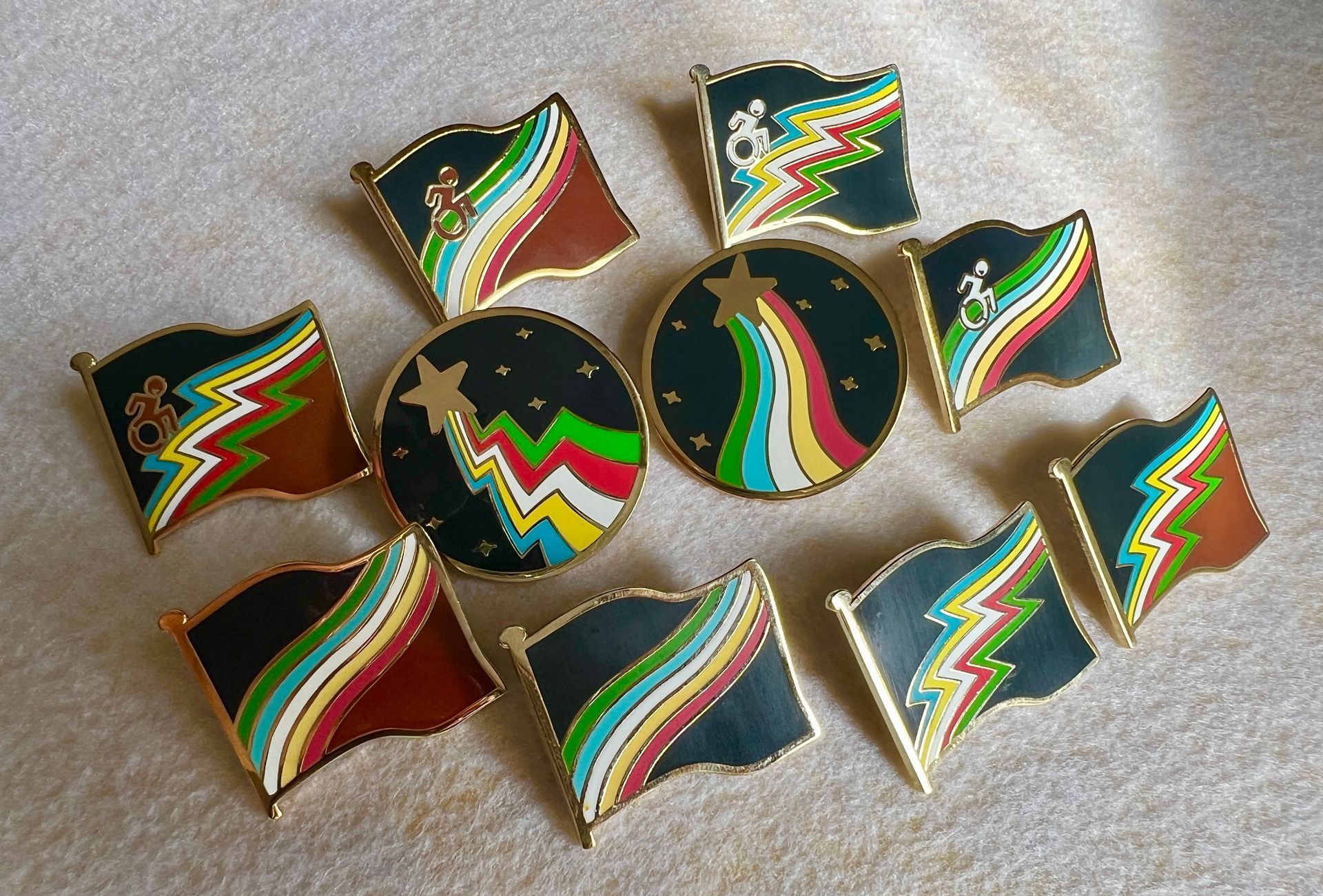 Ten beautiful Progressive Disability Pride Flag pins are on a cream background.  Sunlight shines highlights the gold areas.