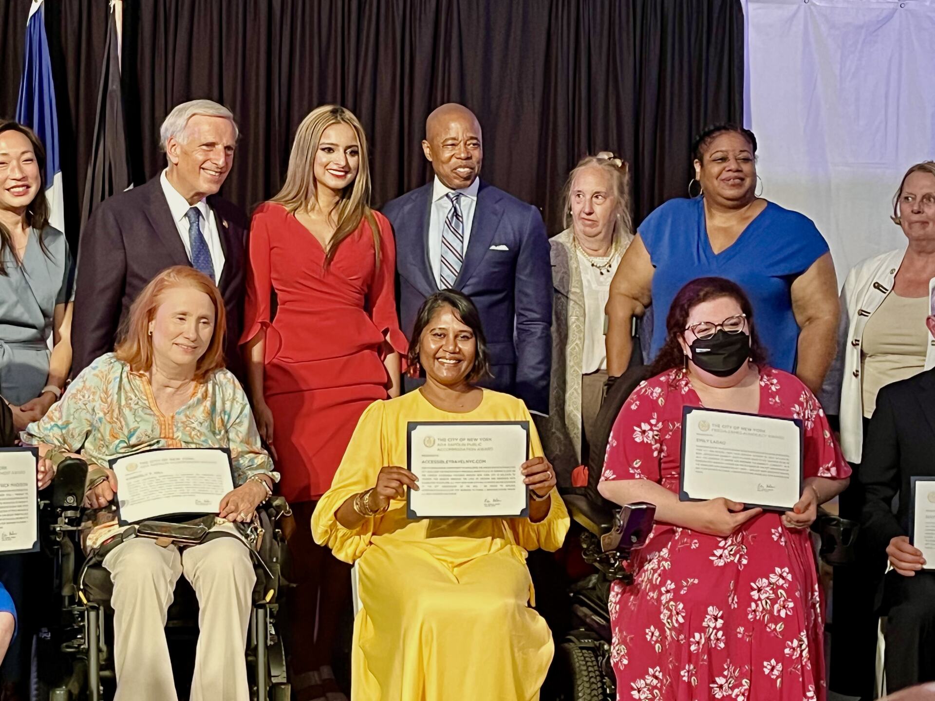 On a stage Kim Hill, Emily Ladau and myself holding our certificates. Several govt officials behind us including Mayor Adams.