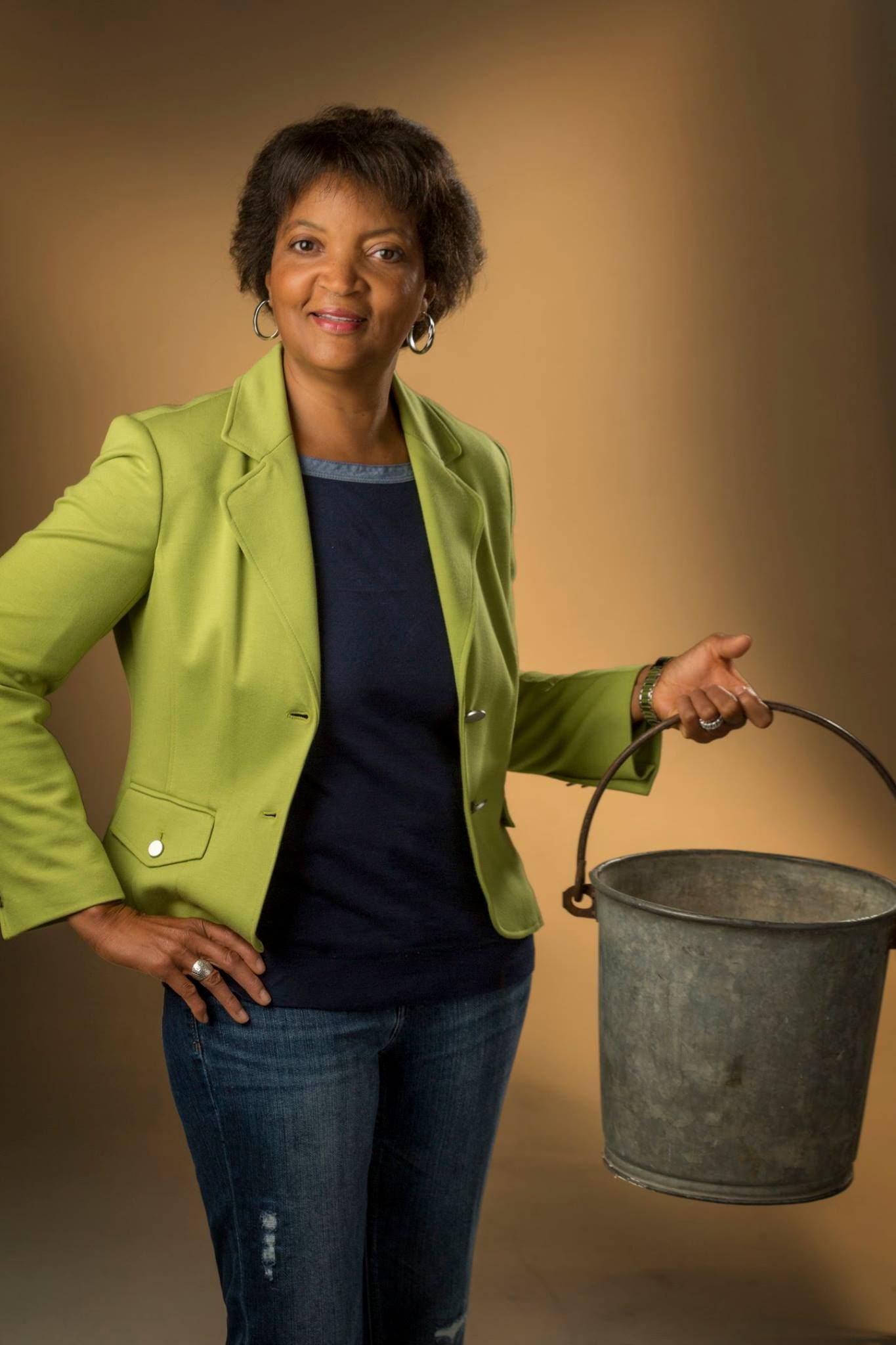 A woman in a green jacket is holding a metal bucket.