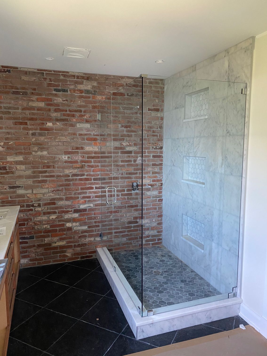 A bathroom with a walk in shower and a brick wall.