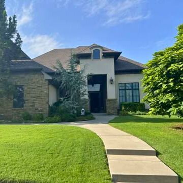 A light-colored house with a stone facade, arched entryway, and a winding sidewalk on a grassy lawn.