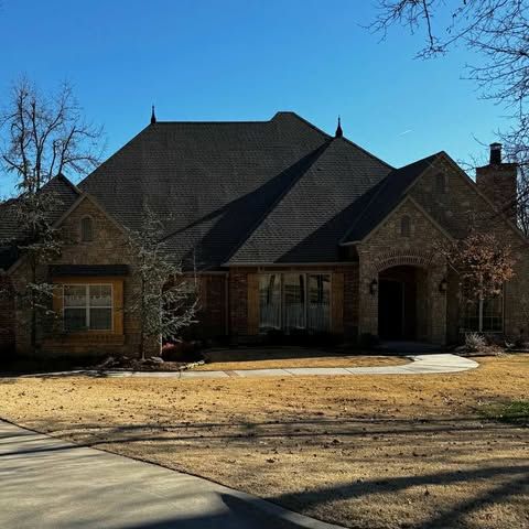 Brick and stone house with a dark roof and a clear blue sky.