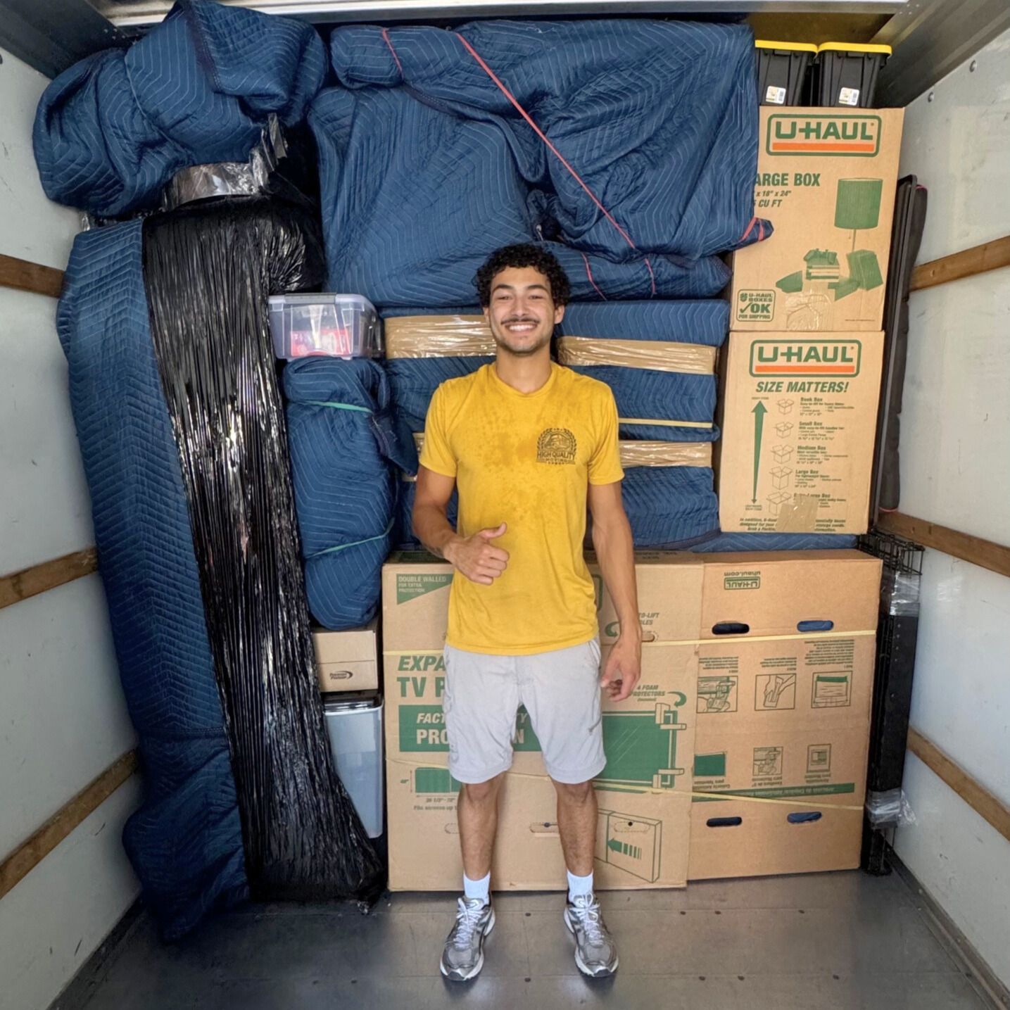 Man standing in a U-Haul truck filled with boxes and wrapped furniture, giving a thumbs-up.