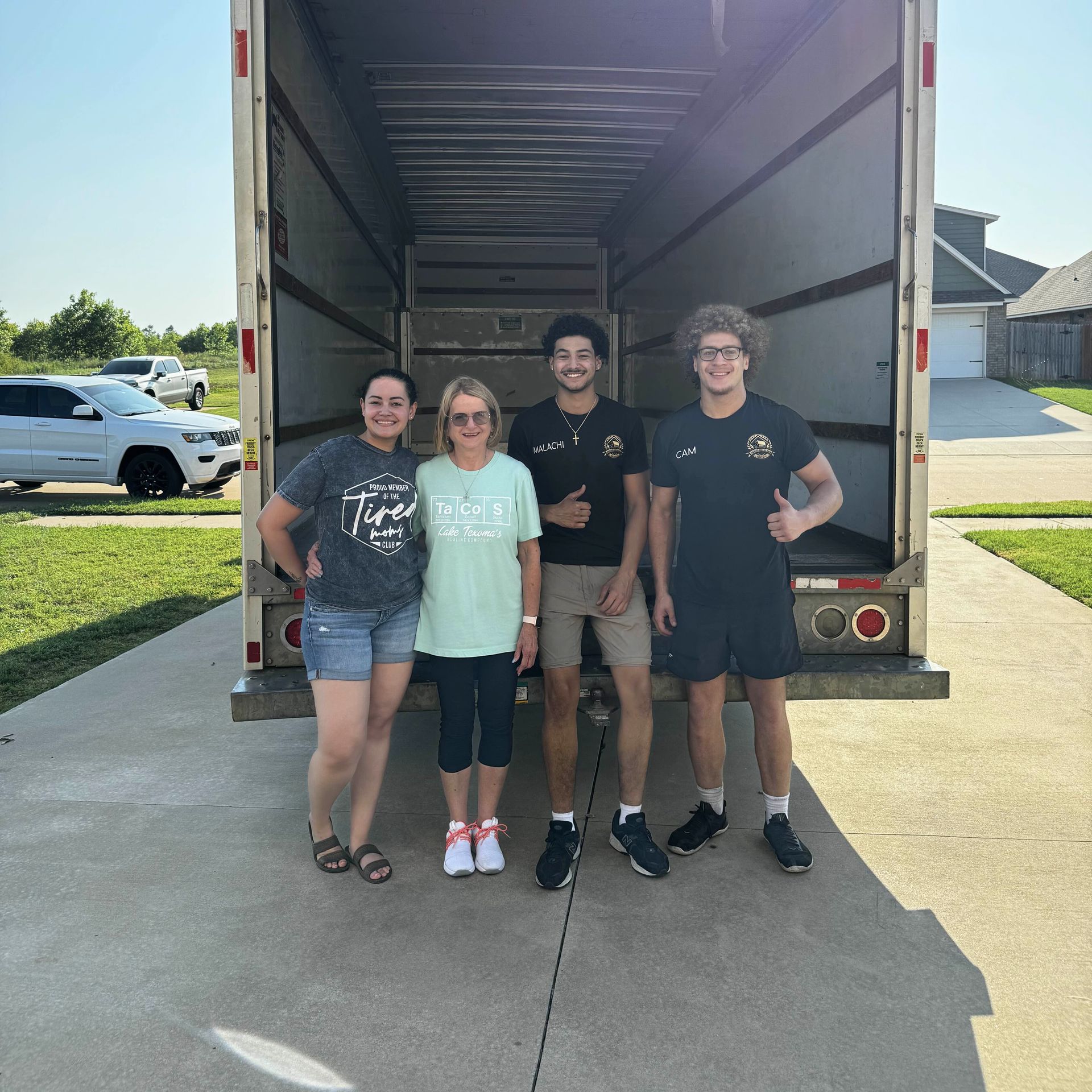 Four people standing in front of an empty moving truck on a sunny day. They are smiling and giving thumbs-up.