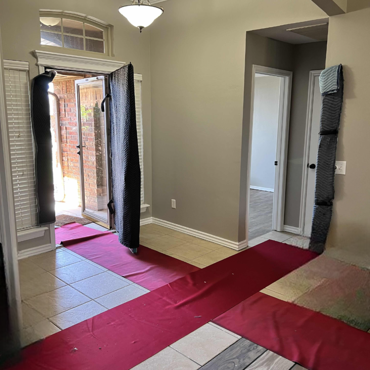 Red carpet covers flooring inside a home. Doorways are draped with padded protection, and a door is open.