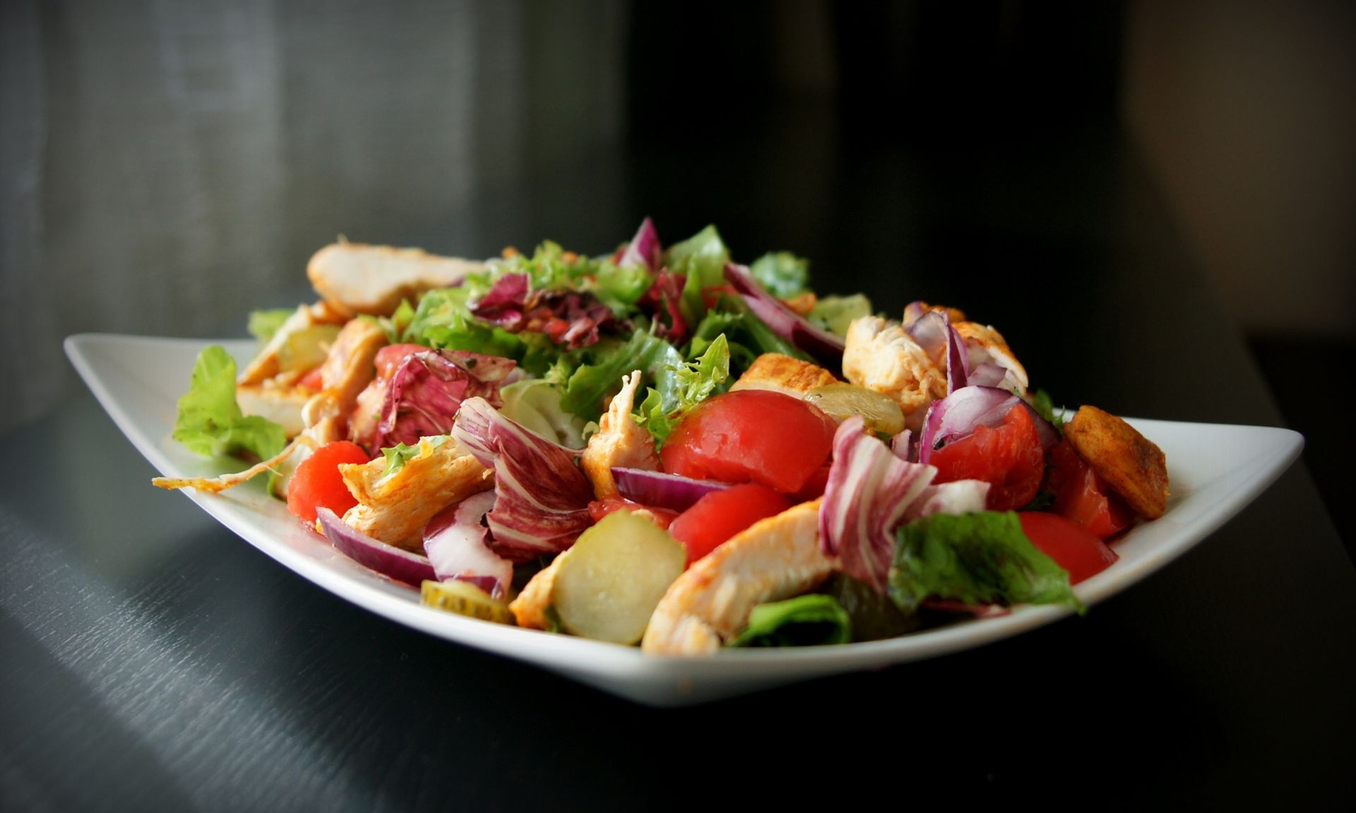 Een wit bord met daarop een salade van kip, tomaten, uien en sla.