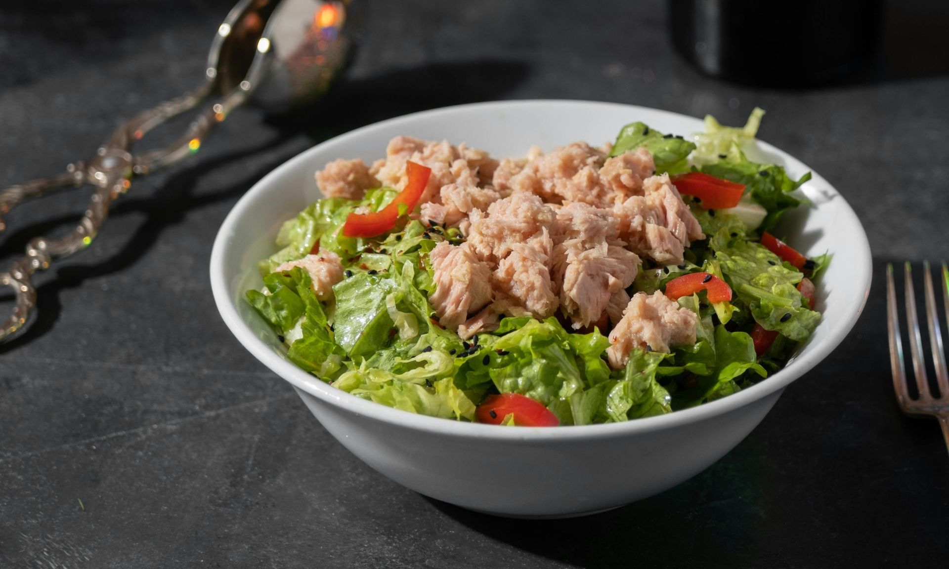 Een kom tonijnsalade met sla, tomaten en een vork op tafel.