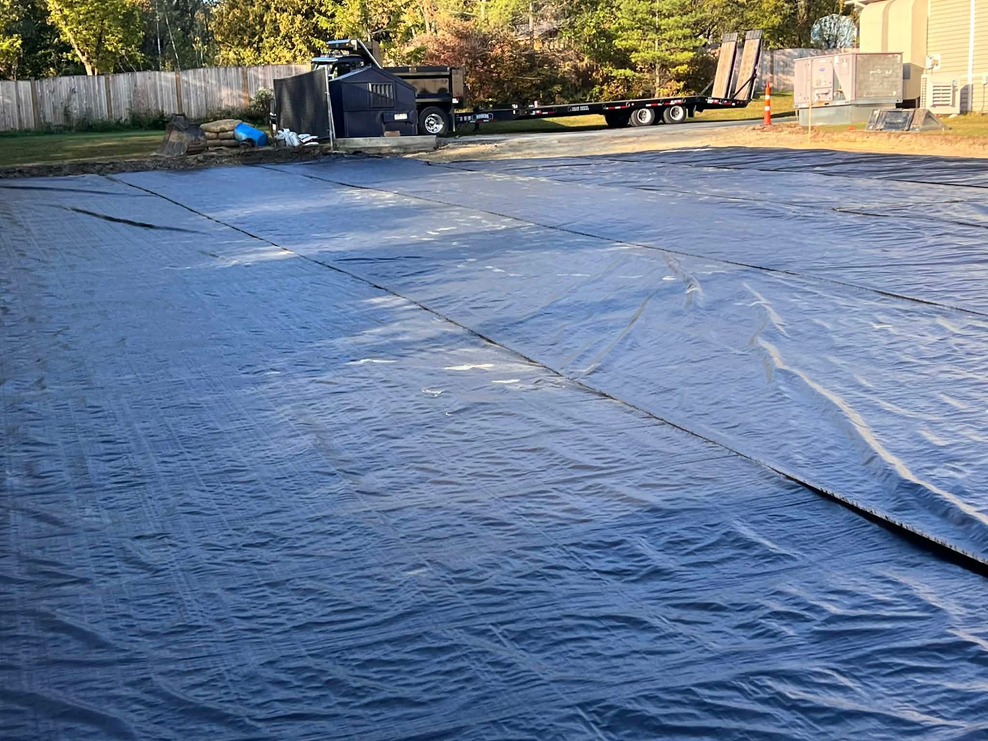 Black pool cover on a backyard pool. A vehicle and trailer are in the background.