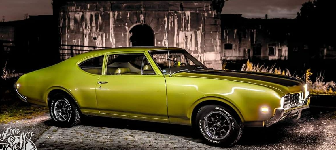 Een groene oldsmobile-cutlass supreme staat geparkeerd voor een gebouw.