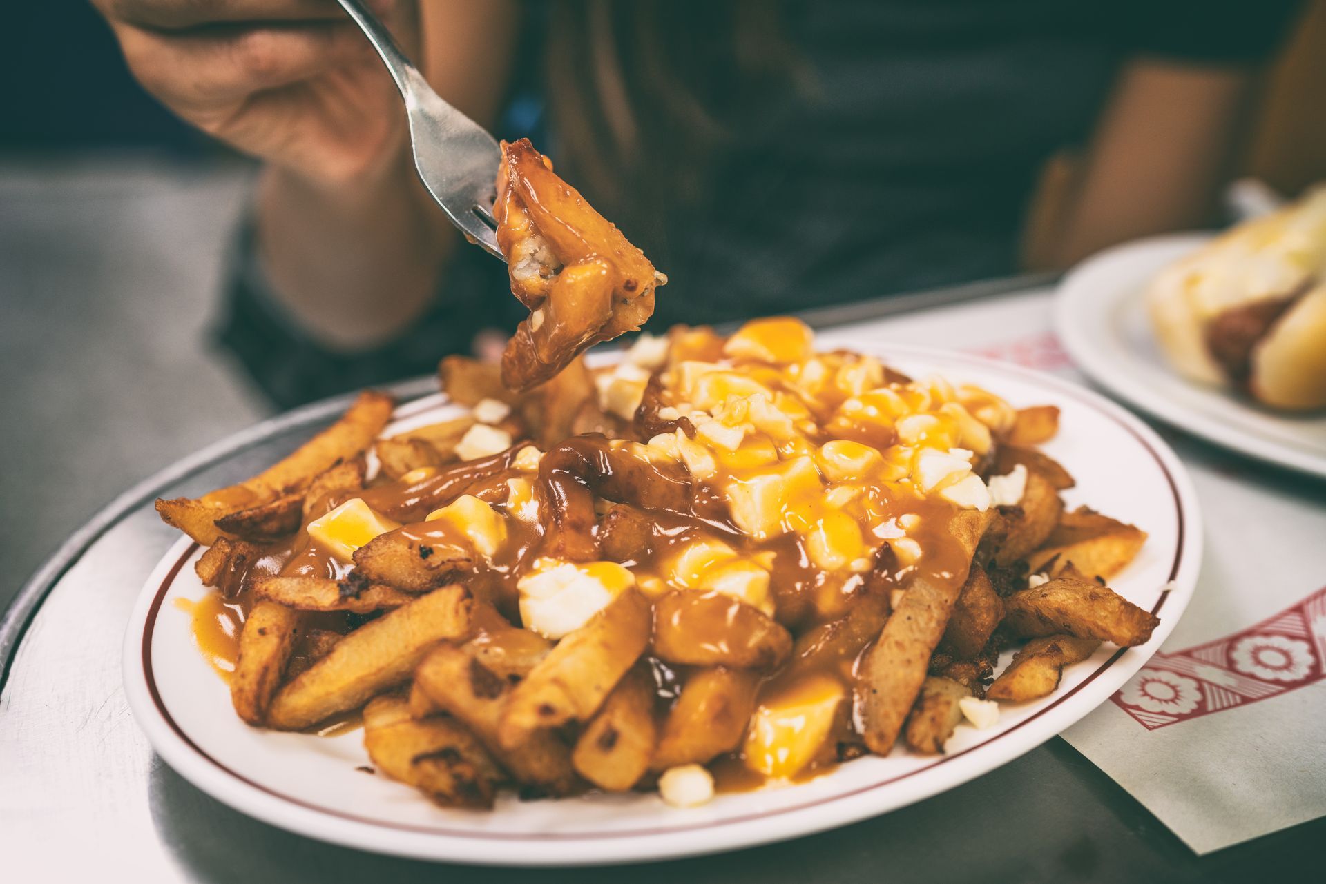Plate of fries topped with cheese and sauce, with a hand lifting a bite on a restaurant table