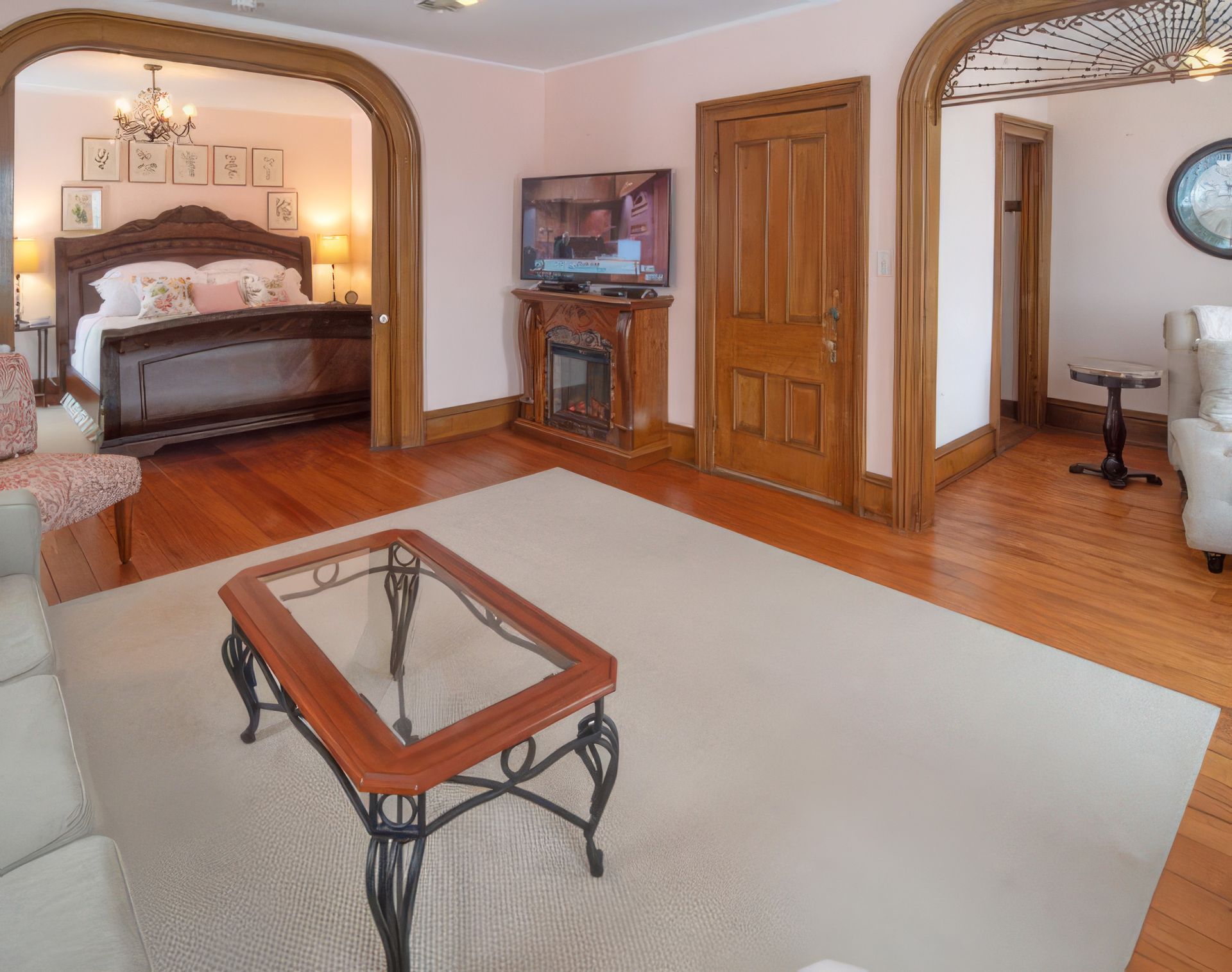 Bedroom with a four-poster bed, TV, wooden doors, and a glass coffee table on a beige rug.