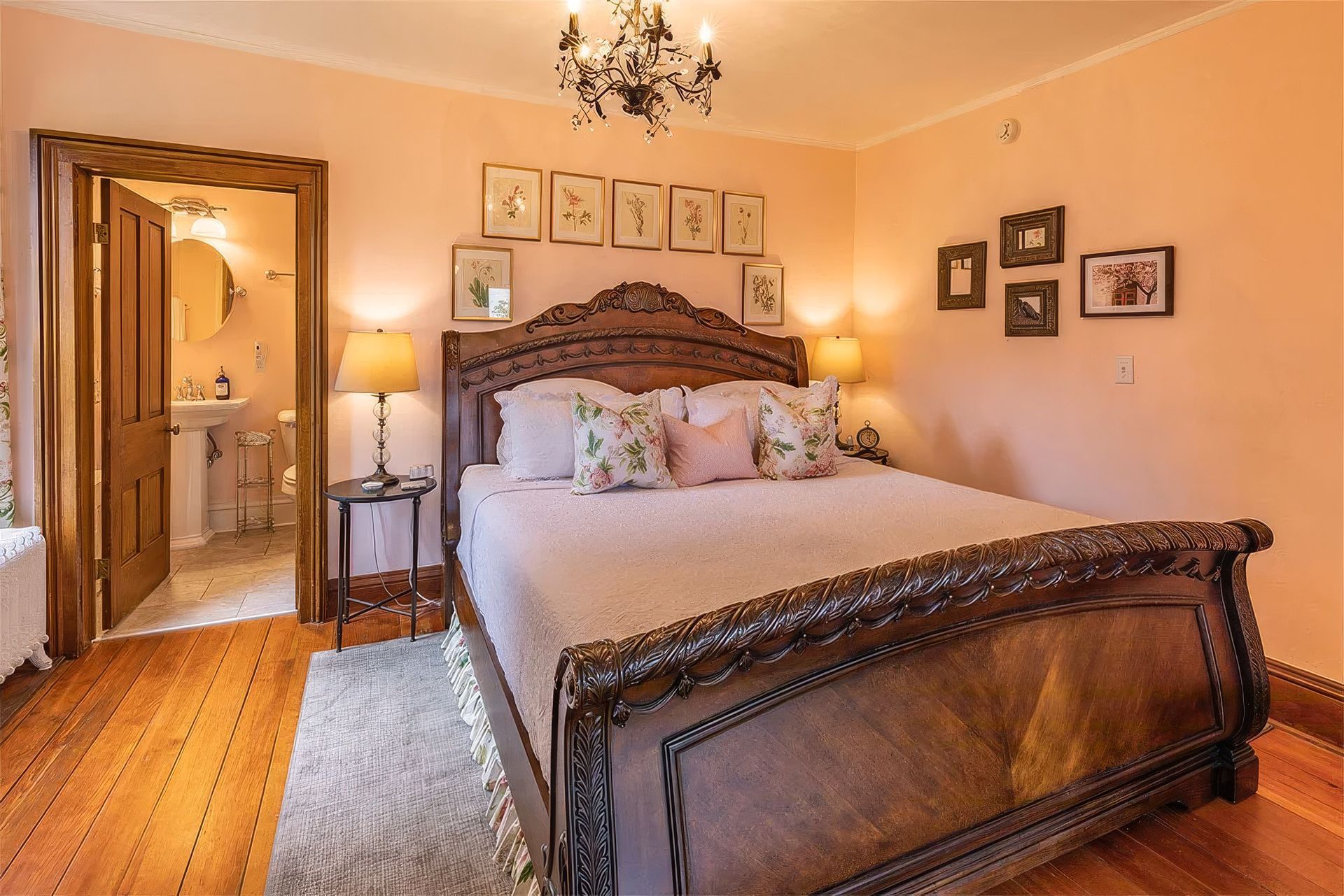 Cozy peach bedroom with ornate bed, chandelier, lamp, and open doorway to hall